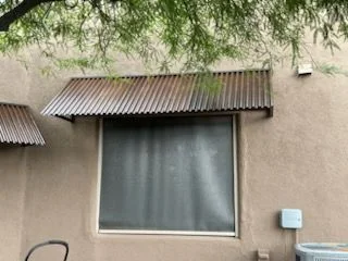 Rusted corrugated steel awning over a window on a stucco house