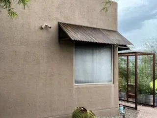 Corrugated steel awning over a window at the corner of a stucco house