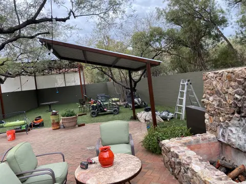 Steel shade structure over a backyard patio with a stone fireplace