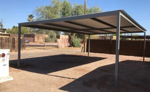 Large gray freestanding steel carport over a dirt lot with a steel fence behind