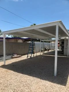 White freestanding steel carport over a gravel lot beside a block wall