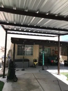 Dark steel patio cover with a metal roof over a concrete back patio