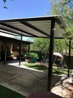 Dark steel patio cover with a metal roof seen from a backyard with lawn and trees