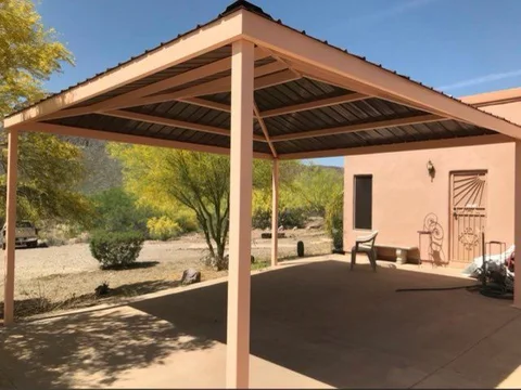 Freestanding steel shade structure with a metal roof over a concrete slab beside a desert home
