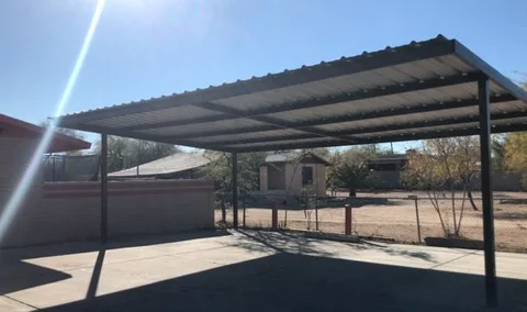Freestanding steel shade cover with a metal roof over a concrete slab, desert yard behind
